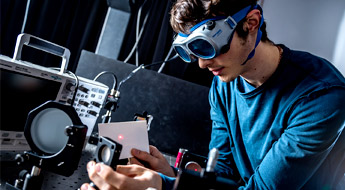 Male student wearing goggles aims laser in optics lab.