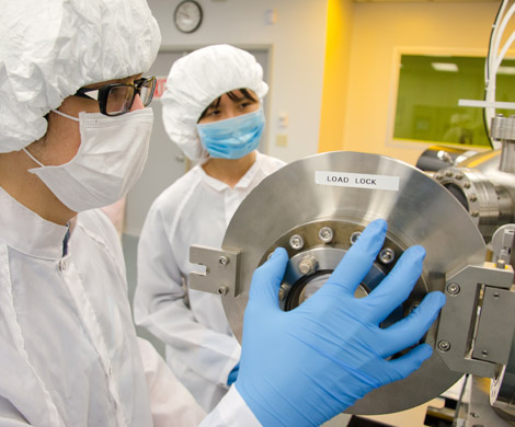 Two students in clean room attire use equipment in the micro- and nano-technology lab.