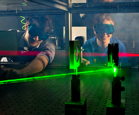 Two male students wearing goggles work with lasers in optics laboratory.