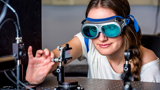 Female student wearing goggles makes adjustment to device.