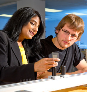 Dr. Kirtley manipulates device in physics lab as male student looks on.