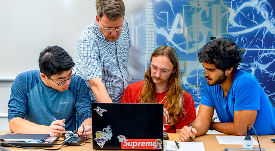 Students discussing with faculty in front of laptop.