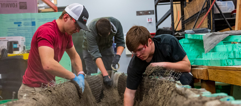 Three students work on the concrete canoe in the BIC.