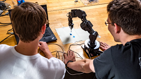 Two students observe as their robotic arm applies paint to paper.