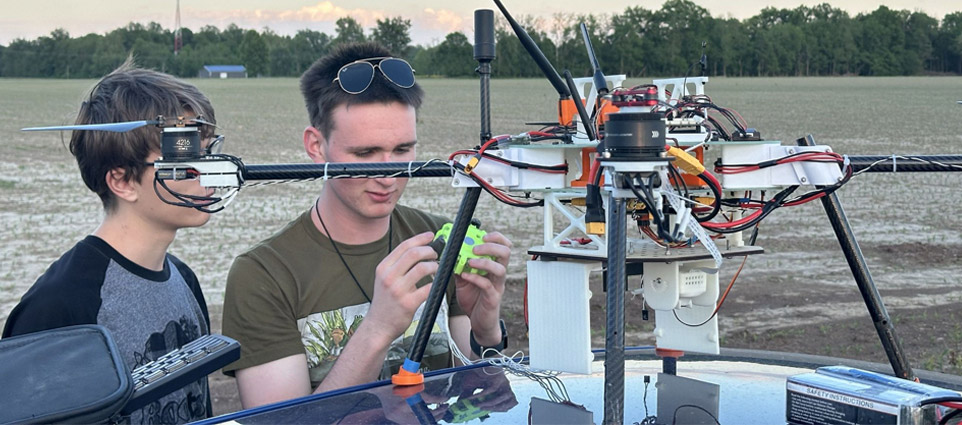 Two students work on a drone in a field.