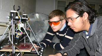 Two students use a 3D printing device.