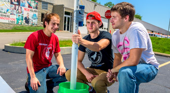Three male students kneel with solar oven project.