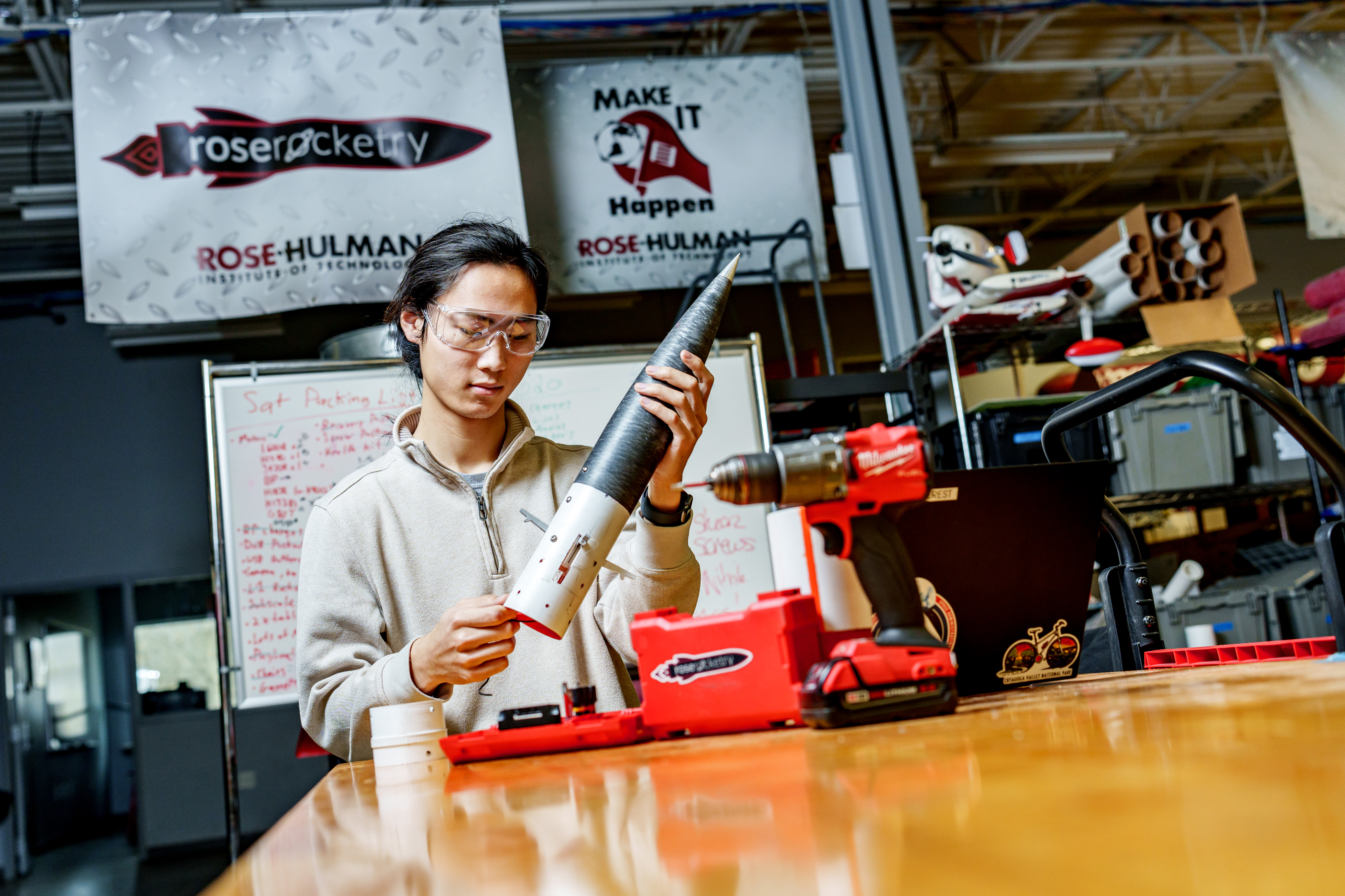 Student works on rocket in front of Rose Rocketry banner.