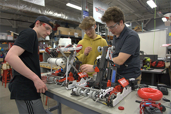 Three students work on a robot on a table in the BIC.
