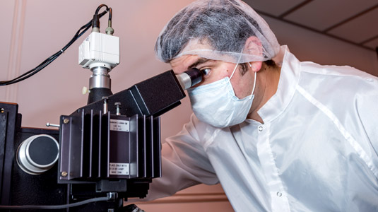 Male in clean room attire uses device to view solar cells.