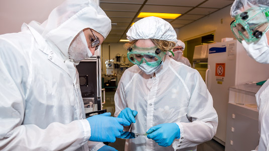 Individuals in clean room attire examine solar cells.