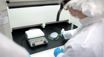 People in clean room attire examine a metal disc.