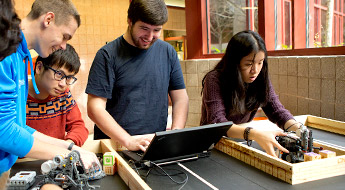 !Male and female students use a laptop to set up robots on a table.