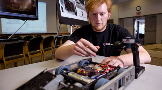 A student manipulates a low-profile wheeled robot.