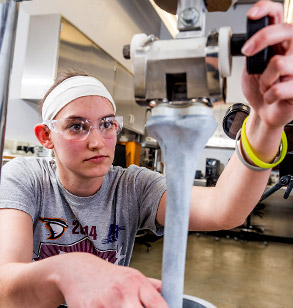 Female student wearing goggles works with apparatus