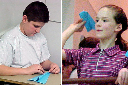 A young male student folds a paper airplane; a young female student begins to throw a paper airplane.