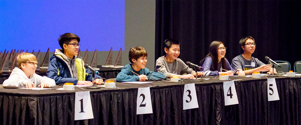 View from balcony as math contest students sit at a table on stage in the Hatfield Hall auditorium