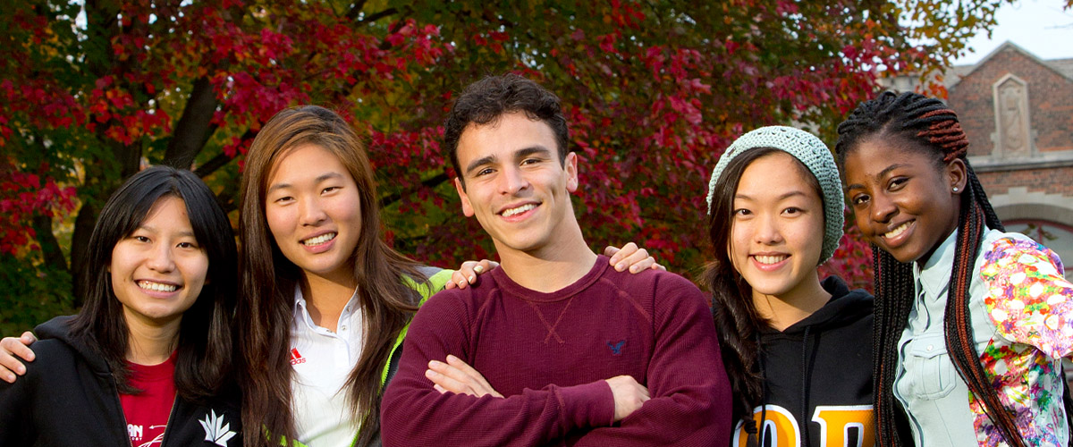 Smiling female student holding her arms out to her sides against a beautiful sky at dusk.