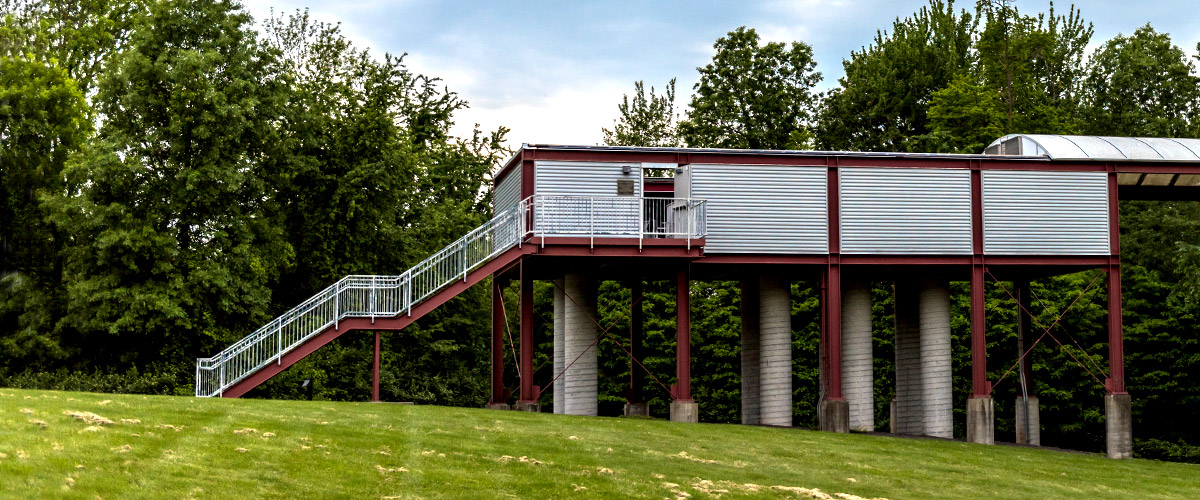 A side view of the shoebox-shaped Oakley Observatory, which sits high on concrete and iron pillars with a long staircase leading to the observatory area.