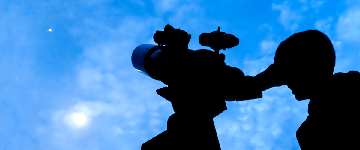 Silhouette of a student looking through a telescope at a bright planet in the dark blue sky high over Oakley Observatory. 