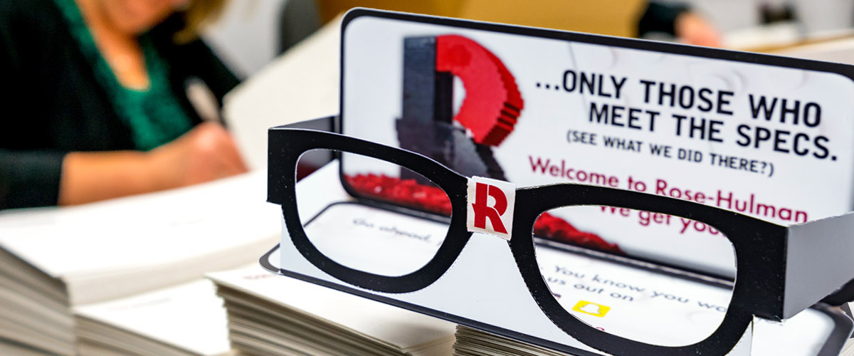 Image shows a pair of cardboard costume “nerd” eyeglasses of the sort delivered to all students who were accepted to attend Rose-Hulman. The glasses include the Rose-Hulman “R” on the bridge and were accompanied by a card stating: “You’re Different. So Are We.”