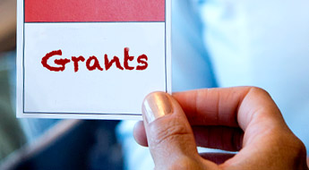 !Image shows a female student’s hand as it holds a small red and white card reading ' Grants.'