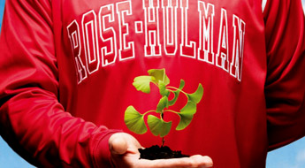 ! Image shows a student wearing a red Rose-Hulman sweatshirt and holding a small green plant with its roots in rich black soil.