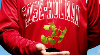 ! Image shows a student wearing a red Rose-Hulman sweatshirt and holding a small green plant with its roots in rich black soil.