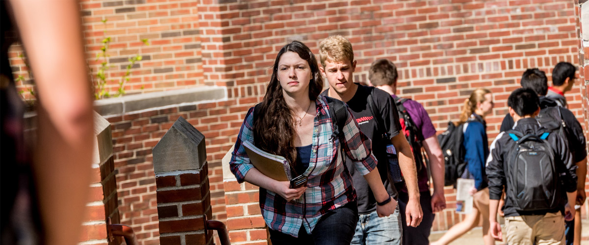 Image shows students walking outdoors between classes in the quad area outside of Moench Hall.