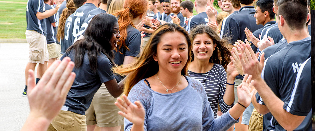 Image shows female freshmen smiling while running between two lines of resident assistants and other current Rose-Hulman students receiving high fives. It’s part of the tradition of welcoming freshmen to campus.
