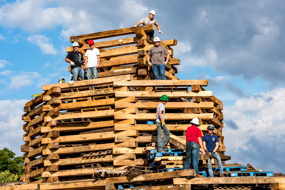 students in hard hats atop the bonfire structure as it's being built