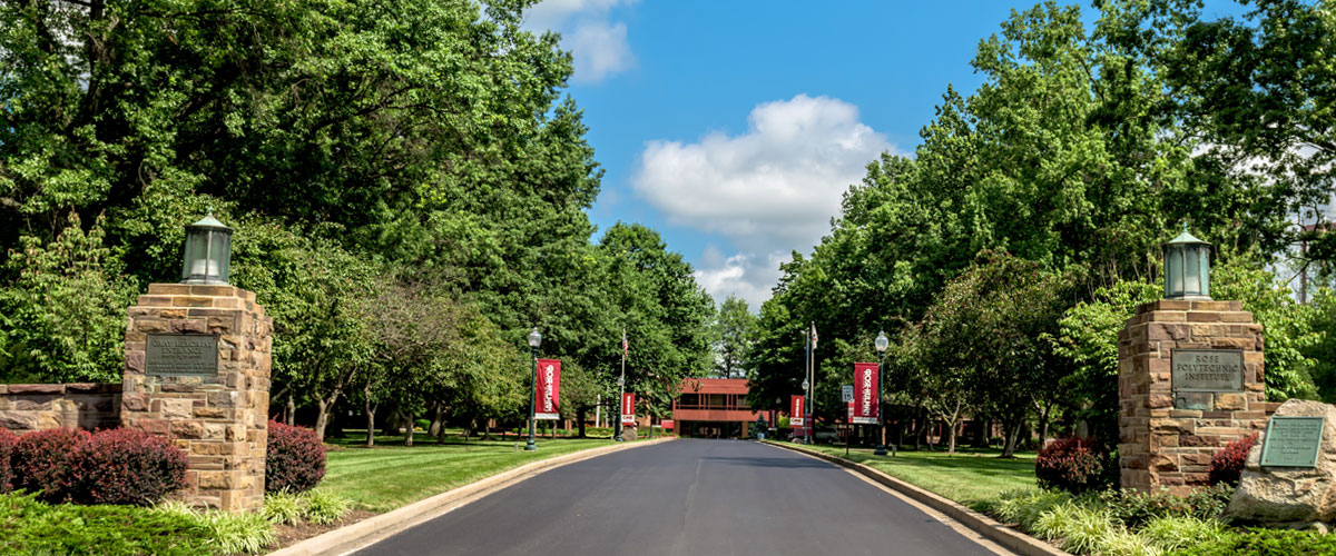 The main entrance to Rose-Hulman Institute of Technology with Hadley Hall in the distance, leafy trees, and blue sky.  