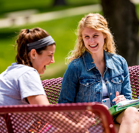 Two female Rose-Hulman students sit on a bench and laugh.
