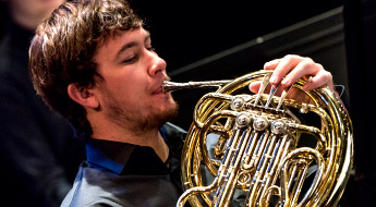 A male student member of the Rose-Hulman orchestra playing the French horn.