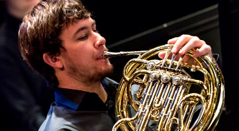 !A male student member of the Rose-Hulman orchestra playing the French horn.