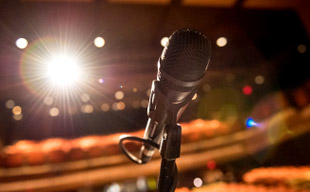 Close-up image of a microphone on the stage of the Hatfield Hall auditorium with a bright stage light and auditorium seats in the background.