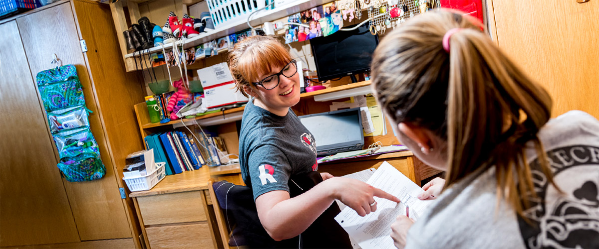 A smiling student points to work on another student’s homework.