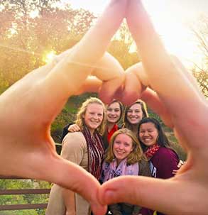 Several members of Alpha Omicron Pi hold their sorority letters in front of Speed Lake. 