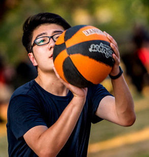 A student prepares to make a  jump shot while playing basketball on an  outdoor basketball court on campus.