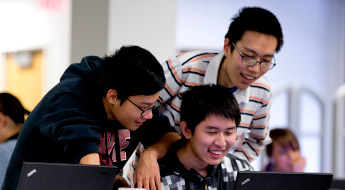 Three smiling students look at laptop computer.