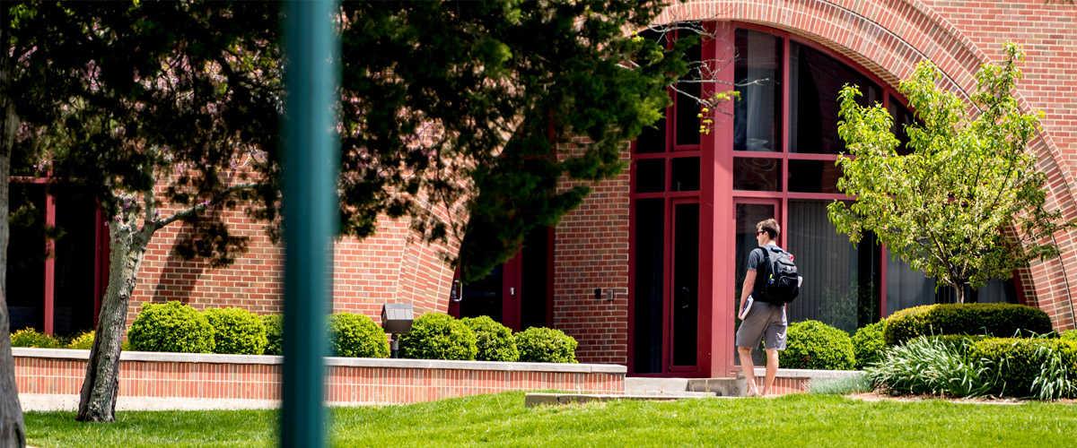 Student walking near the arched entrance to Olin Advanced Learning Center.