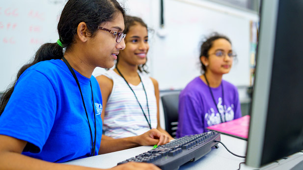 Three young female students working on a computer in a classroom during Connecting with Code.