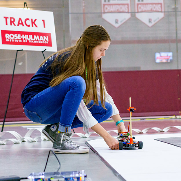 Kneeling girl positions an autonomous vehicle on the track during the competition