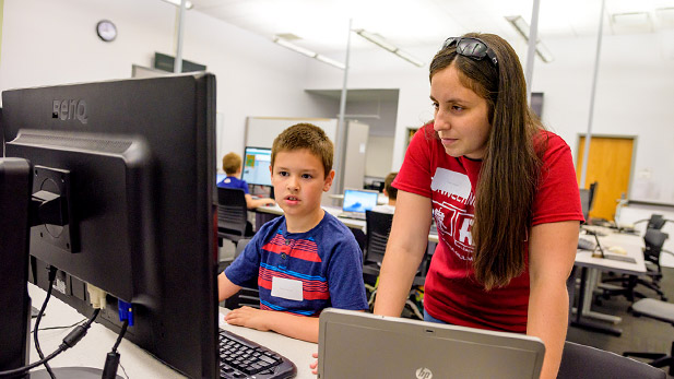 Child works with a college student on a computer