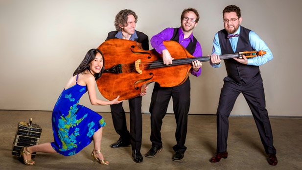 Three smiling men and a woman hold an upright bass. 