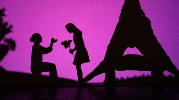 Image of boy and girl in shadow on a large screen in a field. 