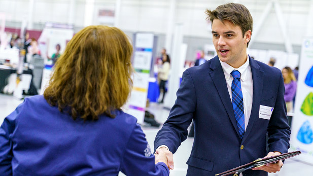 A male student in a jacket and tie shaking hands with a company recruiter.