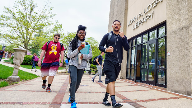 Three students walking on a sunny day outside of the Logan Library. 