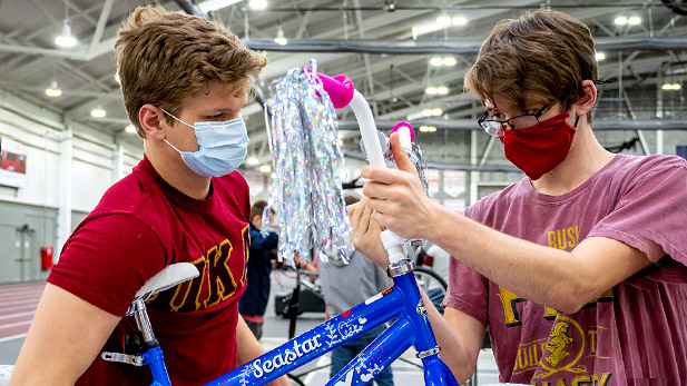 Image shows two students wearing masks assembling a bicycle.