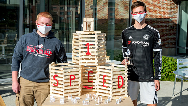 Image shows two students standing with a bonfire model. The model includes lettering saying "Speed 1."
